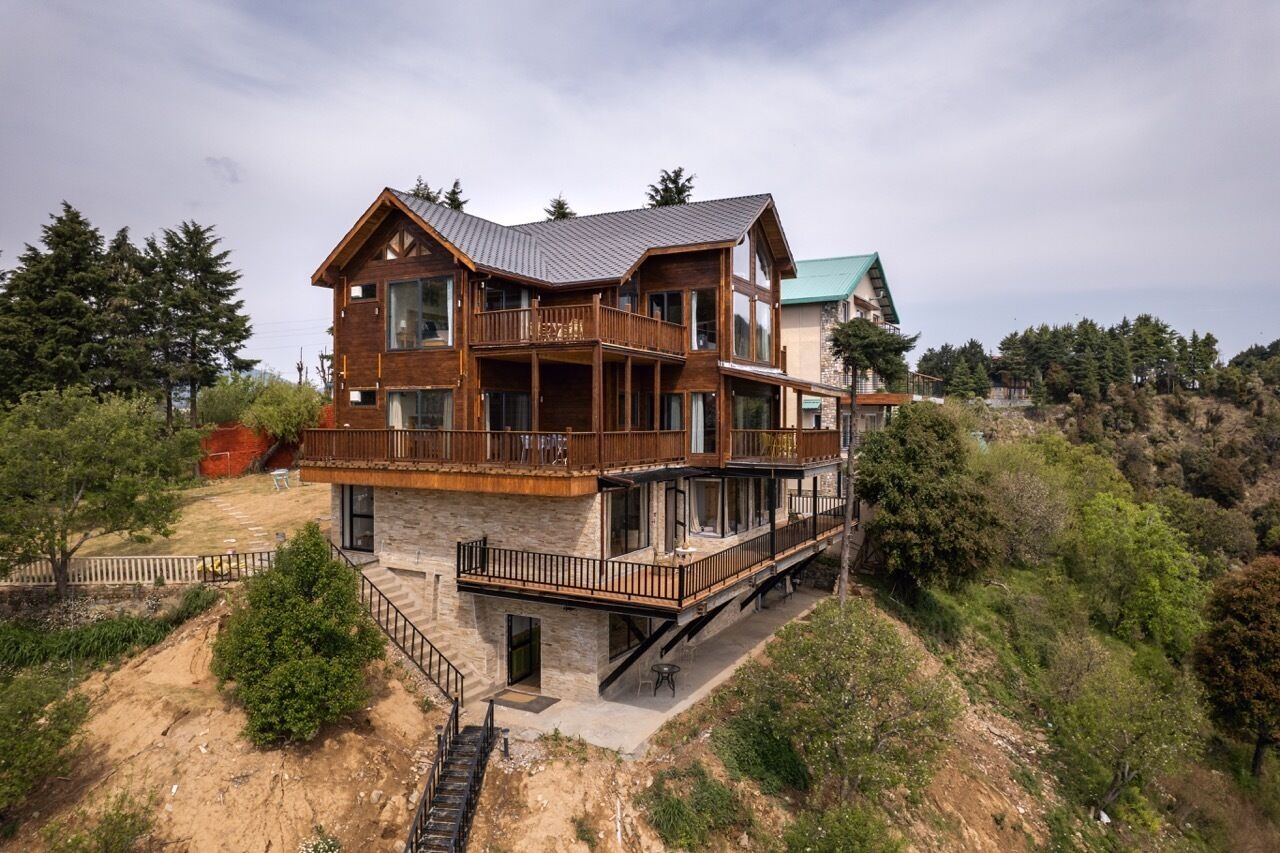 Una casa de madera de varios pisos con balcones, ubicada en una colina rodeada de árboles.