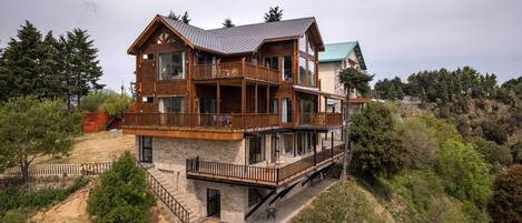 Una casa de madera de varios pisos con balcones, ubicada en una colina rodeada de árboles.
