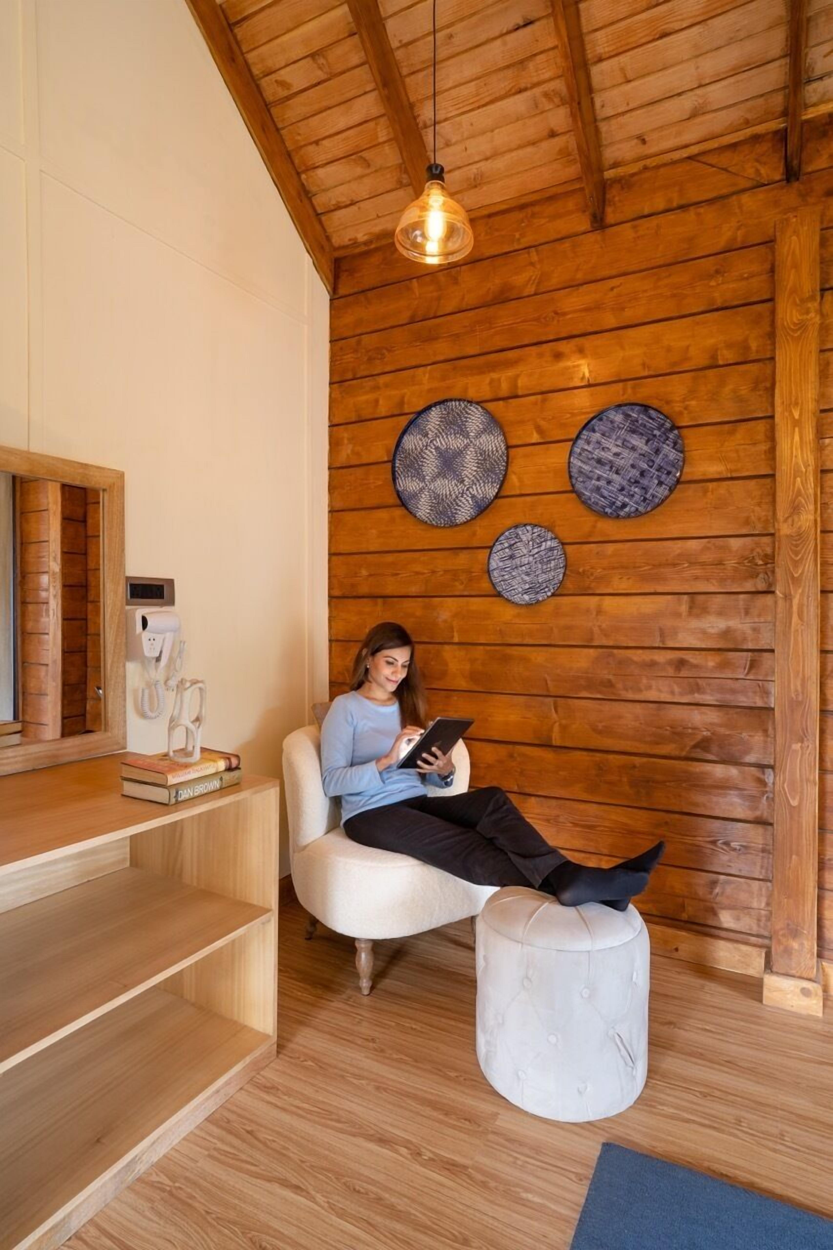 Un interior de madera con una persona sentada en una silla blanca, leyendo un libro.
