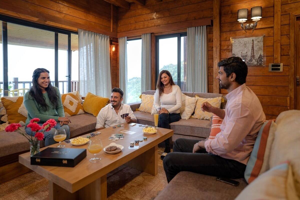 A wooden interior with a sofa set, a coffee table with snacks and drinks, and a view through large windows.