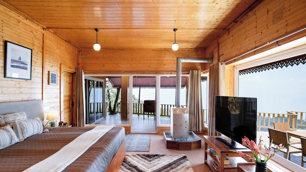 A wooden cabin interior with a bed, TV, and a balcony with a view. - Avalon Cottages Kanatal (Tehri)