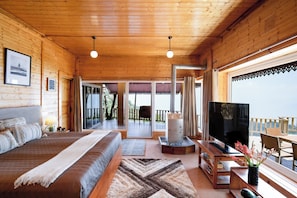 A wooden cabin interior with a bed, TV, and a balcony with a view. - Avalon Cottages Kanatal (Tehri)