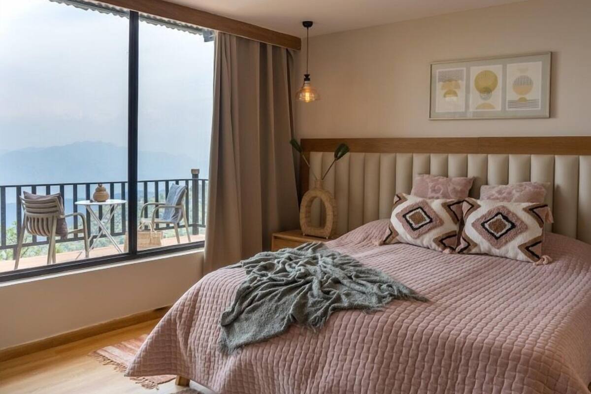 A bedroom with a large bed, a view of the mountains, and a balcony with chairs.