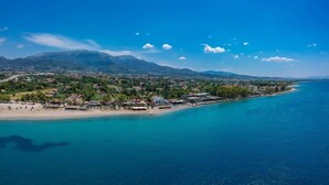 An aerial view of a coastal town with a beach, buildings, and mountains in the background. - Beachfront Rio Escape - Luxurious Coastal Retreat (Rio Patras)