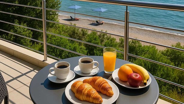 A balcony with a table set for breakfast, overlooking a beach with umbrellas and lounge chairs. - Beachfront Rio Escape - Luxurious Coastal Retreat (Rio Patras)