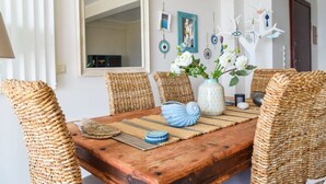 A dining area with a wooden table, woven chairs, and decorative wall art. - Beachfront Rio Escape - Luxurious Coastal Retreat (Rio Patras)