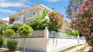 A modern residential building with balconies, surrounded by a white wall and lush greenery. - Beachfront Rio Escape - Luxurious Coastal Retreat (Rio Patras)