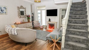 Un salon avec une cheminée, un canapé, un fauteuil, une table basse en verre et un escalier.