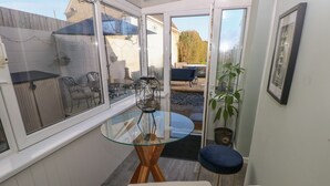 Une pièce de taille modeste, avec une table en verre, un fauteuil rembourré, une plante en pot et un tableau encadré accroché au mur.