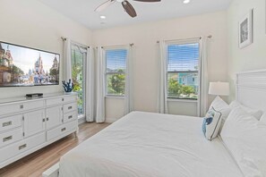 A bedroom with a large bed, a dresser, a flat-screen TV, and a ceiling fan.