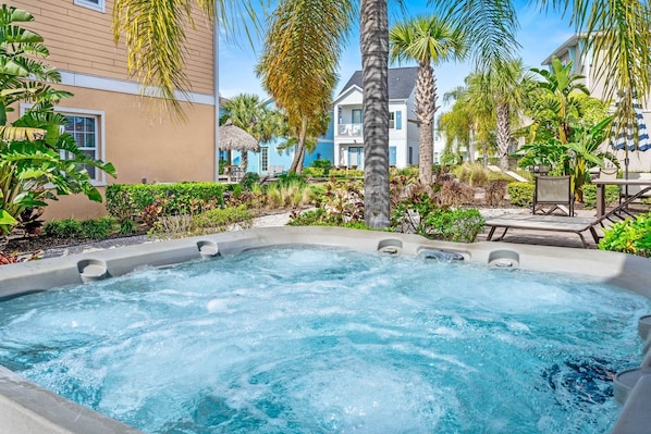A hot tub surrounded by lush greenery and a poolside area with lounge chairs.