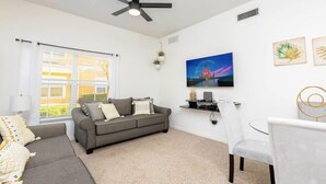 Una sala de estar moderna con un sofá gris, una silla blanca, un ventilador de techo, un televisor y obras de arte en la pared.