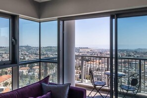 A balcony with a city view, a purple sofa, and two small tables. - Dreamy  2BDR, Unparalleled Views Of The Old City (Jerusalem)