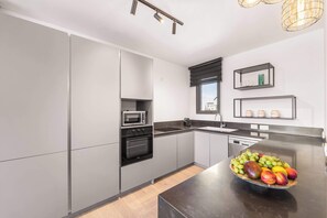 A modern kitchen with grey cabinets, a black countertop, a microwave, an oven, and a fruit bowl on the island.