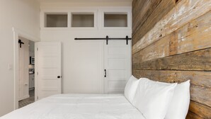 A bedroom with a bed, white walls, a wooden headboard, and a sliding barn-style door. - Abbot 19-Modern Condo, Wood Fireplace, Bikes, Perfect for 4 (Sunriver)