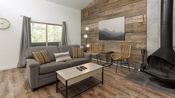 A cozy living room with a sofa, two chairs, a coffee table, a fireplace, and a large window with curtains. - Abbot 19-Modern Condo, Wood Fireplace, Bikes, Perfect for 4 (Sunriver)
