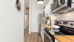 A modern kitchen with white cabinets, a stainless steel refrigerator, a microwave, and a black stove. - Abbot 19-Modern Condo, Wood Fireplace, Bikes, Perfect for 4 (Sunriver)