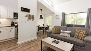 A modern living space with a kitchen, dining area, and a gray sofa with striped pillows. - Abbot 19-Modern Condo, Wood Fireplace, Bikes, Perfect for 4 (Sunriver)