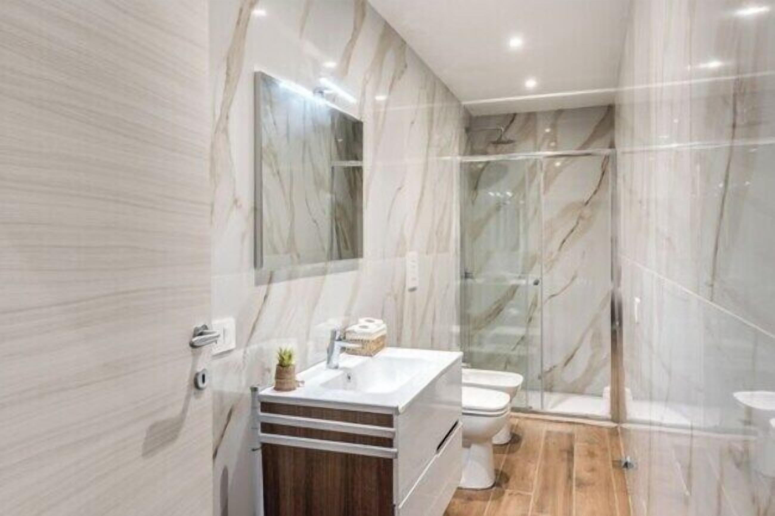 Une salle de bain moderne avec des murs en marbre, une douche en verre et un meuble-lavabo en bois.