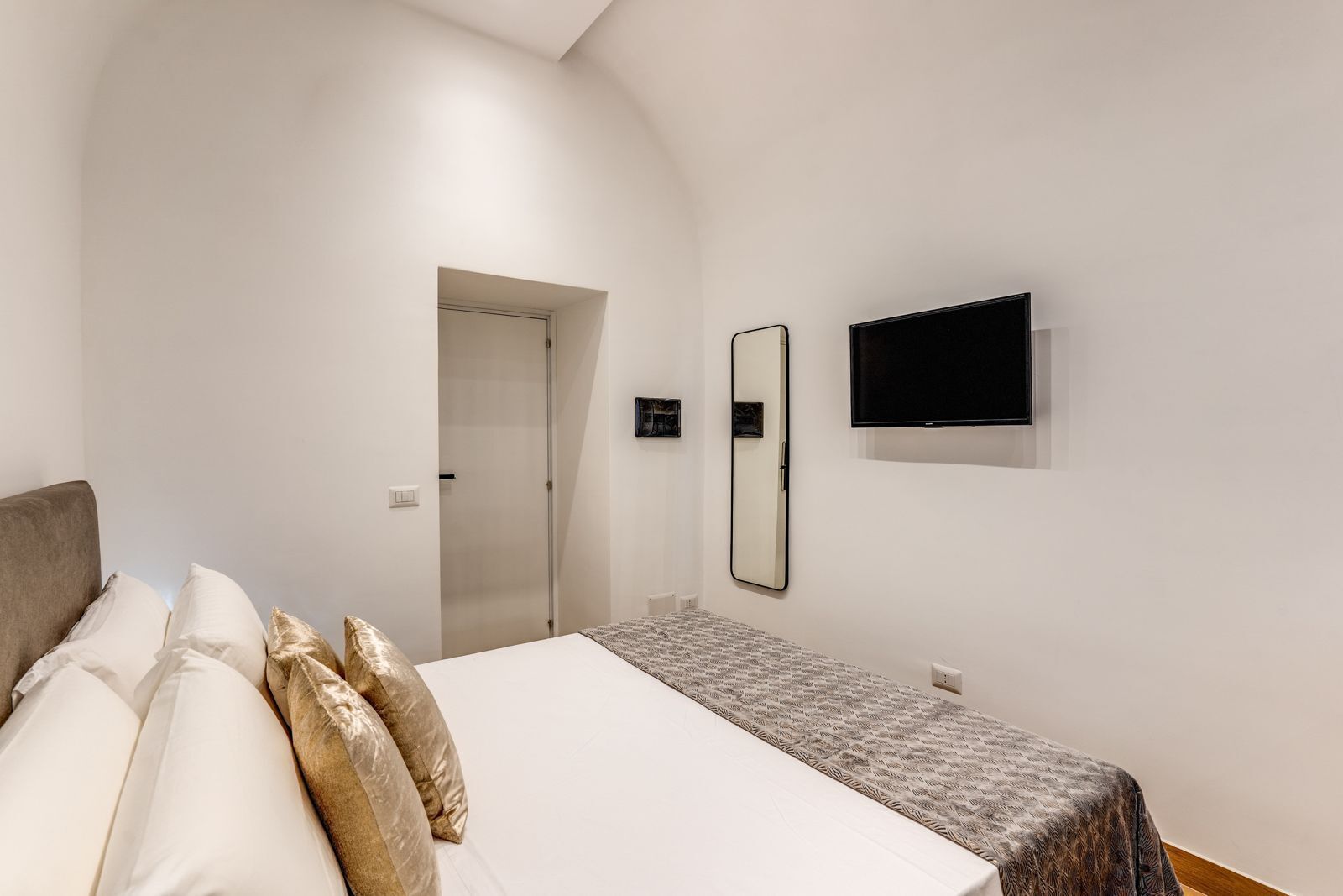 Quarto com cama, televisão, espelho e porta.
