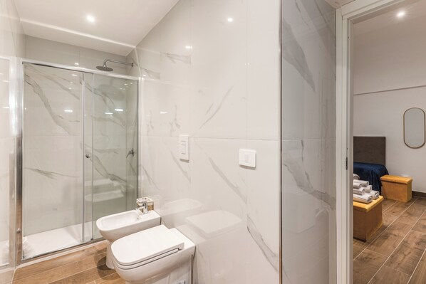 A modern bathroom with a glass-enclosed shower, a toilet, and a bidet.