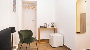 A room with a green chair, a small white refrigerator, a wooden table with a kettle, a lamp, and a mirror. - Domus Partenopea  (Naples)