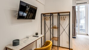 A modern room with a flat-screen TV mounted on the wall, a small table with a remote control, a yellow chair, and a wooden wardrobe with hanging space. - Domus Partenopea  (Naples)