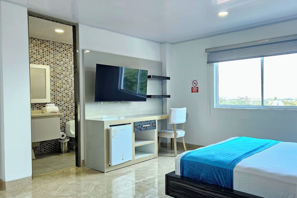 Een hotelkamer met een bed, televisie, bureau, stoel, raam en badkamer.