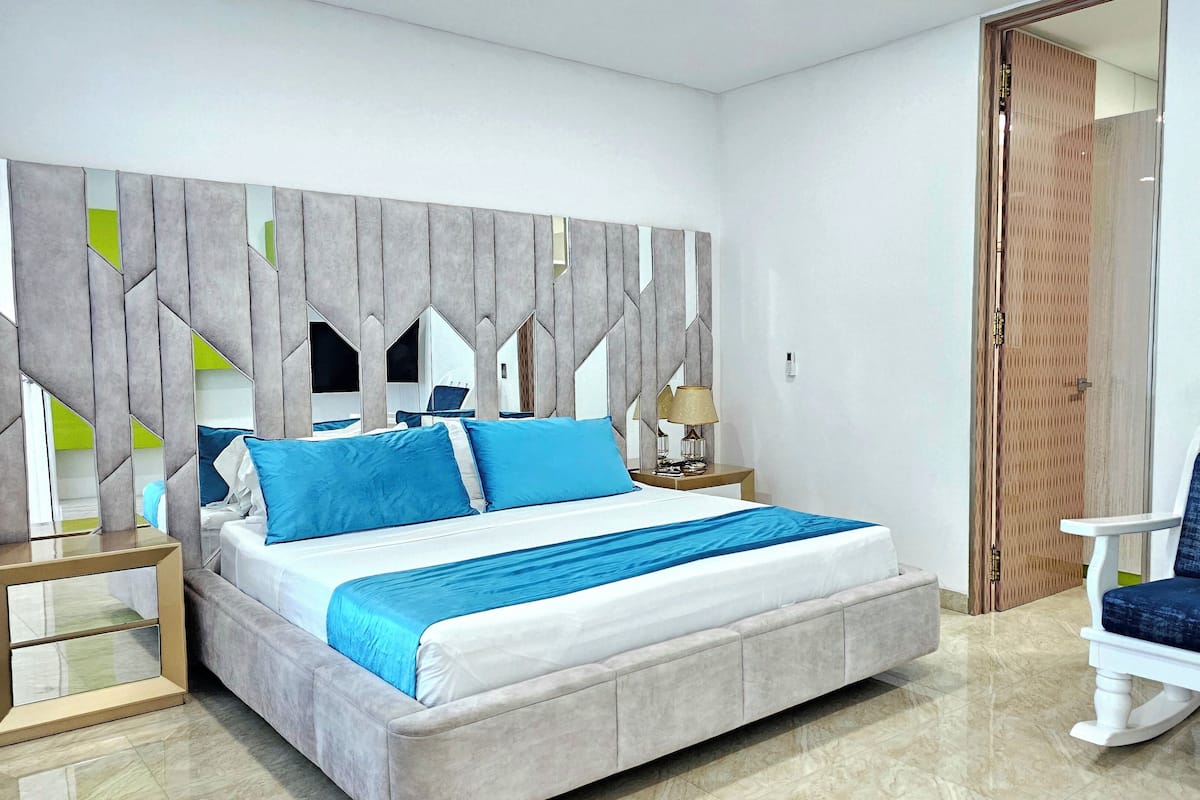 Een moderne slaapkamer met een groot bed, een nachtkastje, een stoel en een decoratief paneel.