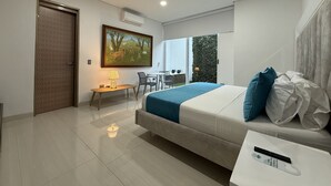 A modern hotel room with a large bed, a desk with a chair, a small table with a lamp, and a painting on the wall. - Lotto Hotel Boutique (Cali)