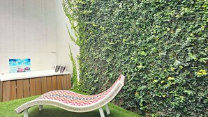 A hammock chair with a colorful woven seat, a wooden bench, and a wall-mounted painting. - Lotto Hotel Boutique (Cali)