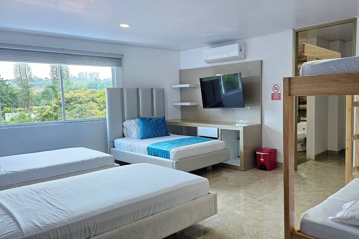 Een hotelkamer met een bed, een bureau met een televisie, een raam met uitzicht en een stapelbed.