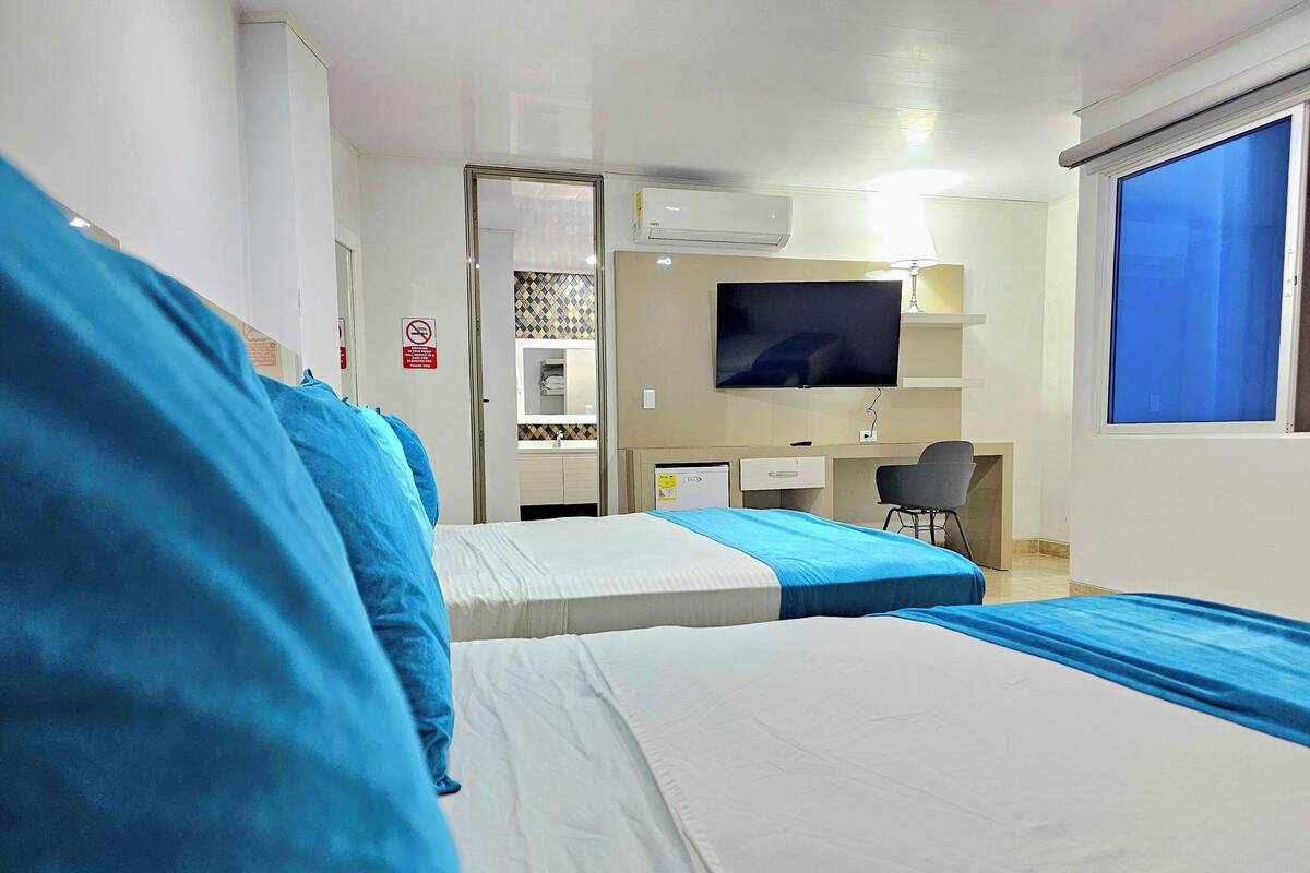 Een hotelkamer met twee bedden, een bureau, een stoel, een televisie en een raam.