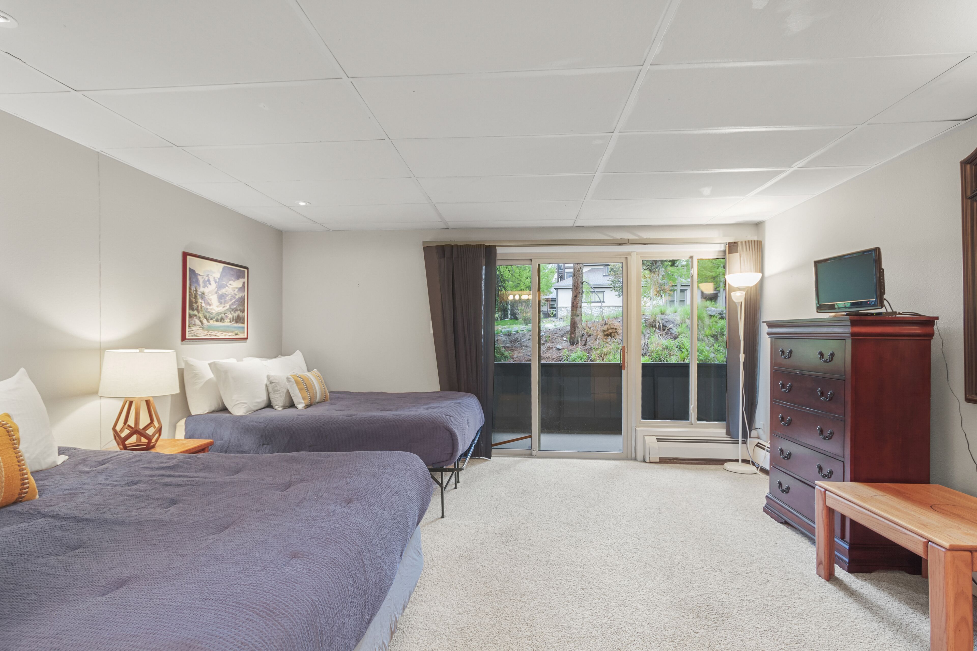 A hotel room with two beds, a dresser, a television, and a view of the outdoors.