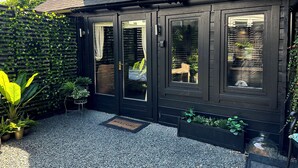 Una casa negra con un reloj en el tejado, una puerta con un ventanal y un felpudo.
