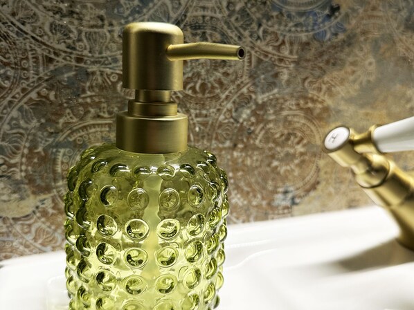 Un baño con un dispensador verde con textura, un grifo dorado y una pared con diseño.