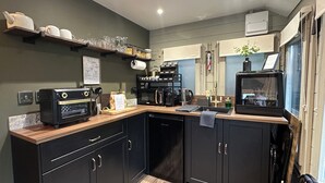 Una cocina compacta con horno integrado, cafetera y microondas. Hay estantes con cristalería y un cartel de bienvenida.