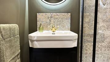 Un bagno con uno specchio tondo, un lavandino bianco e un mobile contenitore nero.
