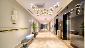 A modern hotel lobby with a marble floor, benches, potted plants, and a sculpture on the wall. - IBOS HOTELS IZMIR (Izmir)
