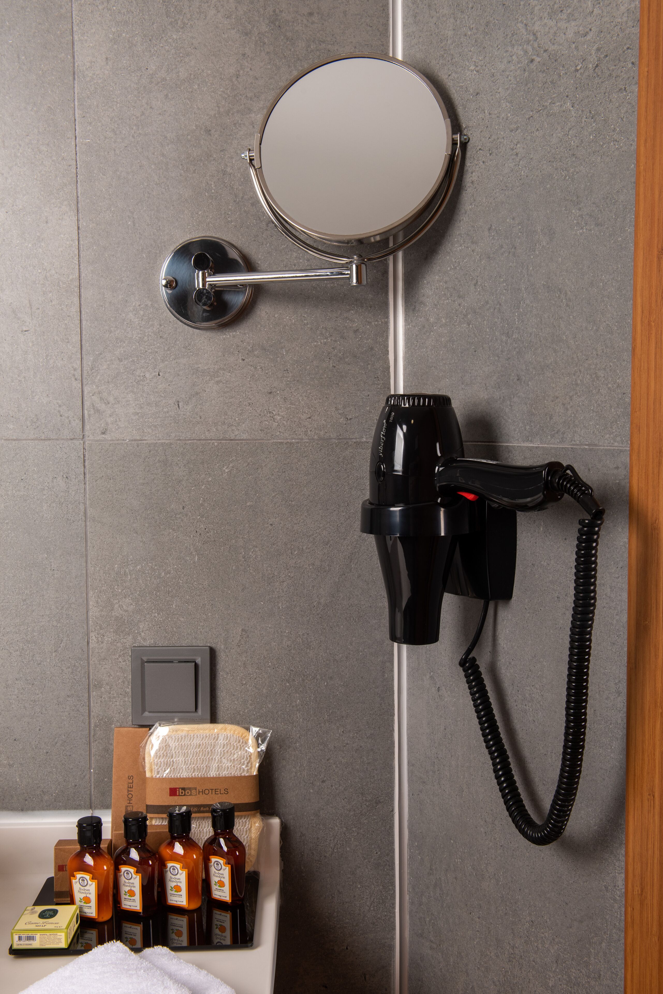 A bathroom with a hairdryer mounted on the wall, a mirror, and a box of toiletries.