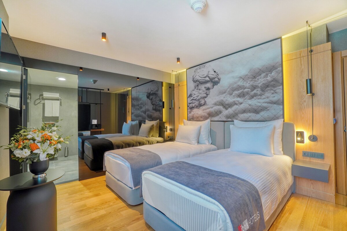 A modern hotel room with two beds, a large mirror, and a painting of clouds on the wall.