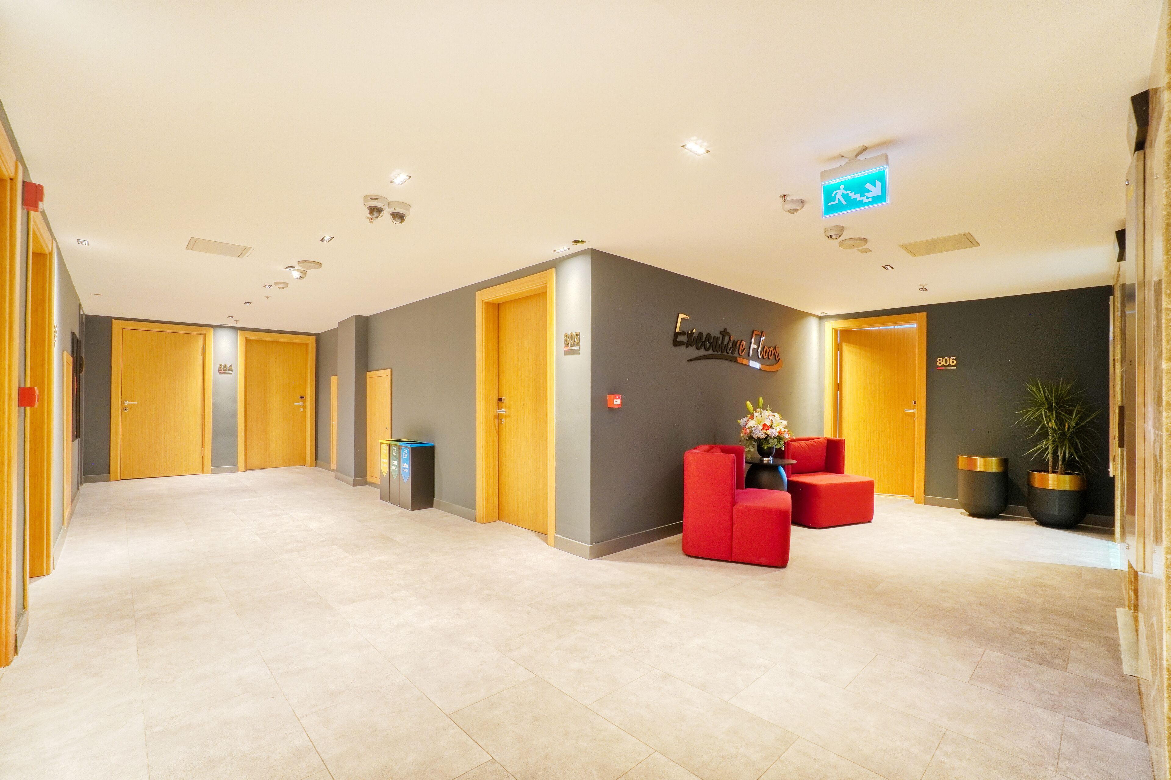 A modern hotel lobby with a reception desk, red seating, and a grey accent wall.