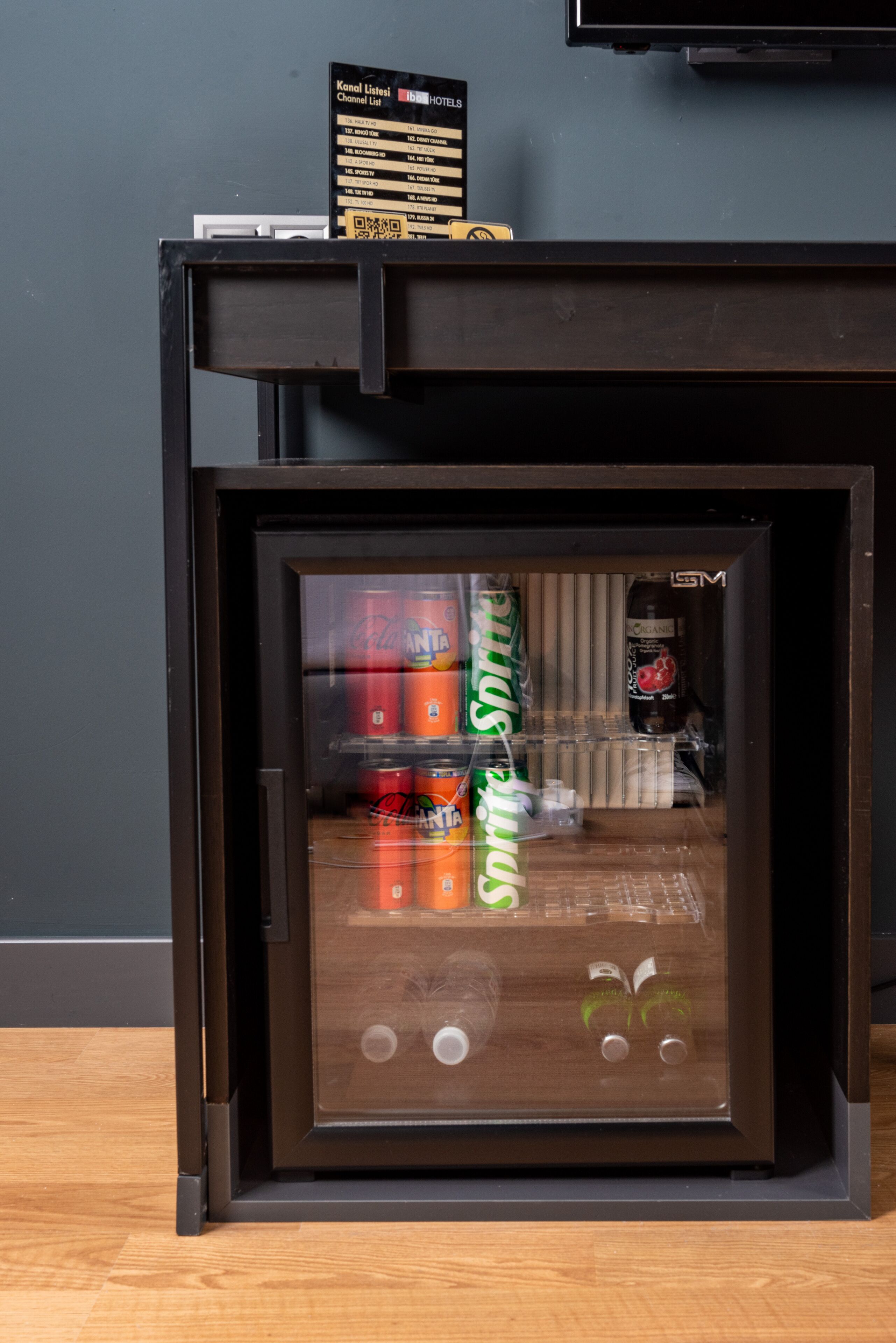 Mini-bar com dispensador de bebidas, incluindo latas de Sprite e outras opções.