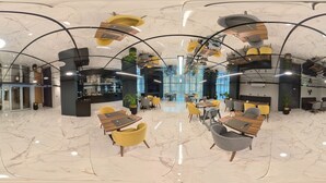 A modern hotel lobby with marble floors, yellow and grey chairs, wooden tables, and a central blue seating area. - IBOS HOTELS IZMIR (Izmir)