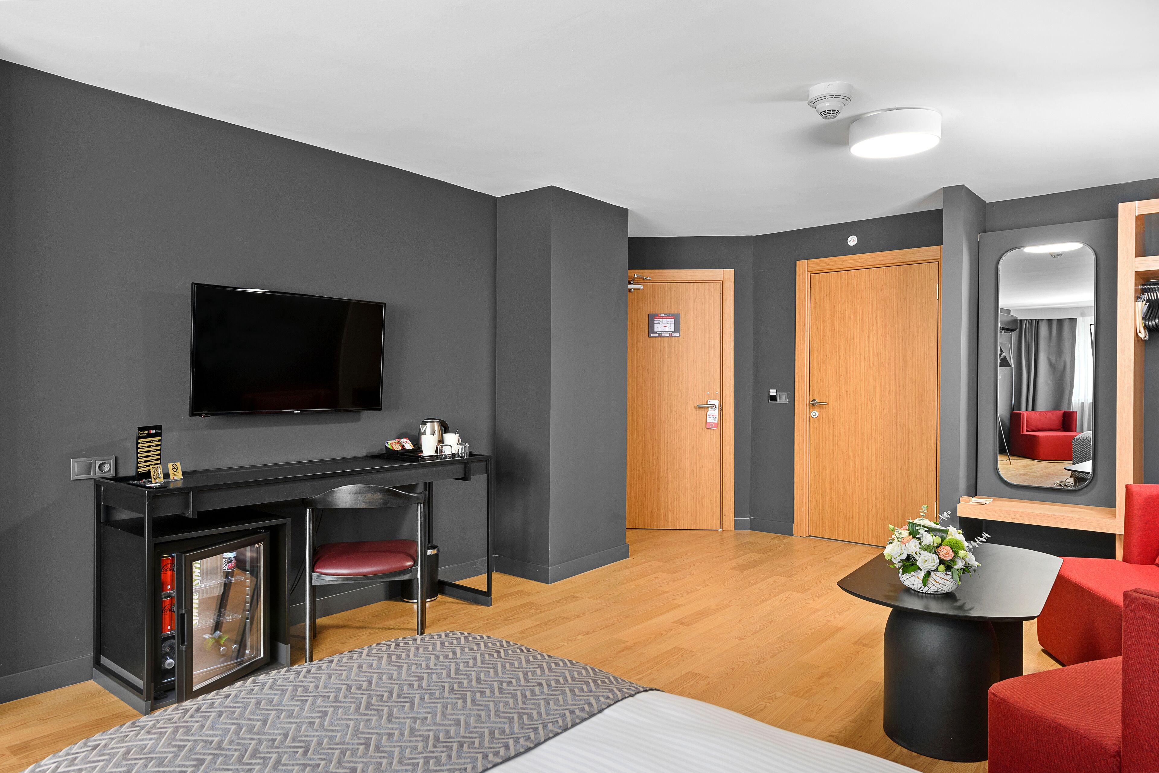Una habitación de hotel moderna con cama, televisión, pequeña cocina, puerta de madera y espejo.