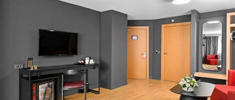 Una habitación de hotel moderna con cama, televisión, pequeña cocina, puerta de madera y espejo.