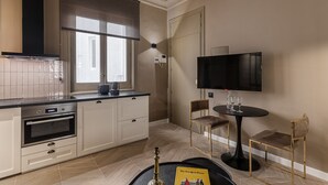 Une cuisine moderne dotée d’un four encastré, d’une grande fenêtre avec stores, d’un téléviseur à écran plat fixé au mur et d’un petit coin repas avec une table et des chaises.
