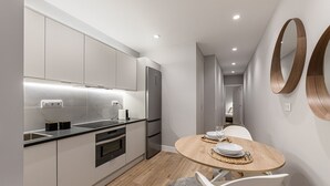 Eine moderne Küche mit integrierten Geräten, ein Essbereich mit rundem Tisch und ein Flur, der zum Schlafzimmer führt.