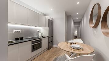 Una cocina moderna con electrodomésticos integrados, un comedor con mesa redonda y un pasillo que lleva a un dormitorio.