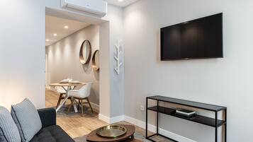 Una sala moderna con sofá, mesa de centro, televisor y comedor con mesa y sillas.